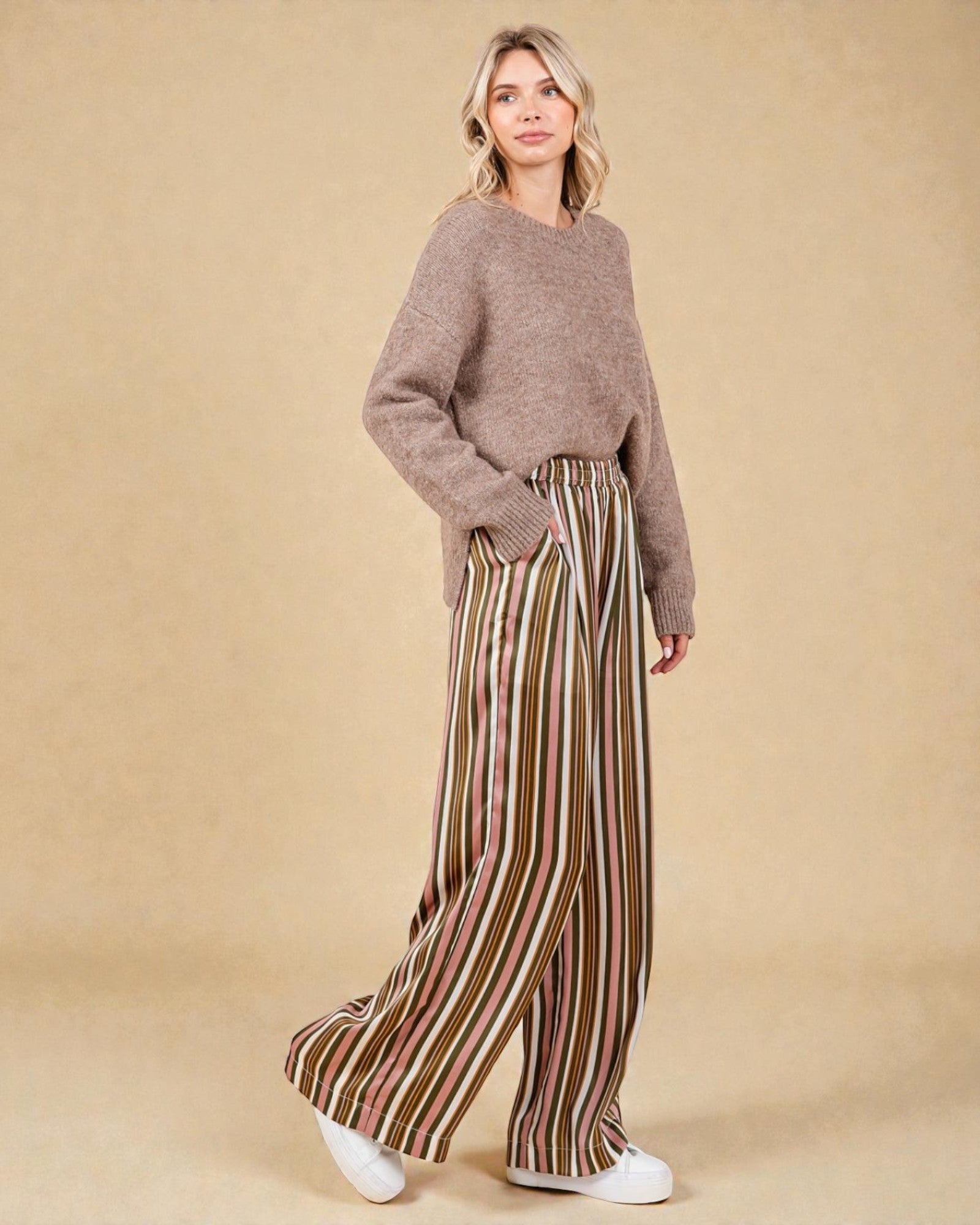Woman wearing a brown sweater and striped pants against a beige background
