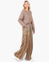 A woman modeling a cozy taupe knit sweater and high-waisted, wide-leg striped trousers with vertical stripes in brown, green, beige, and white, paired with white sneakers against a plain white background.