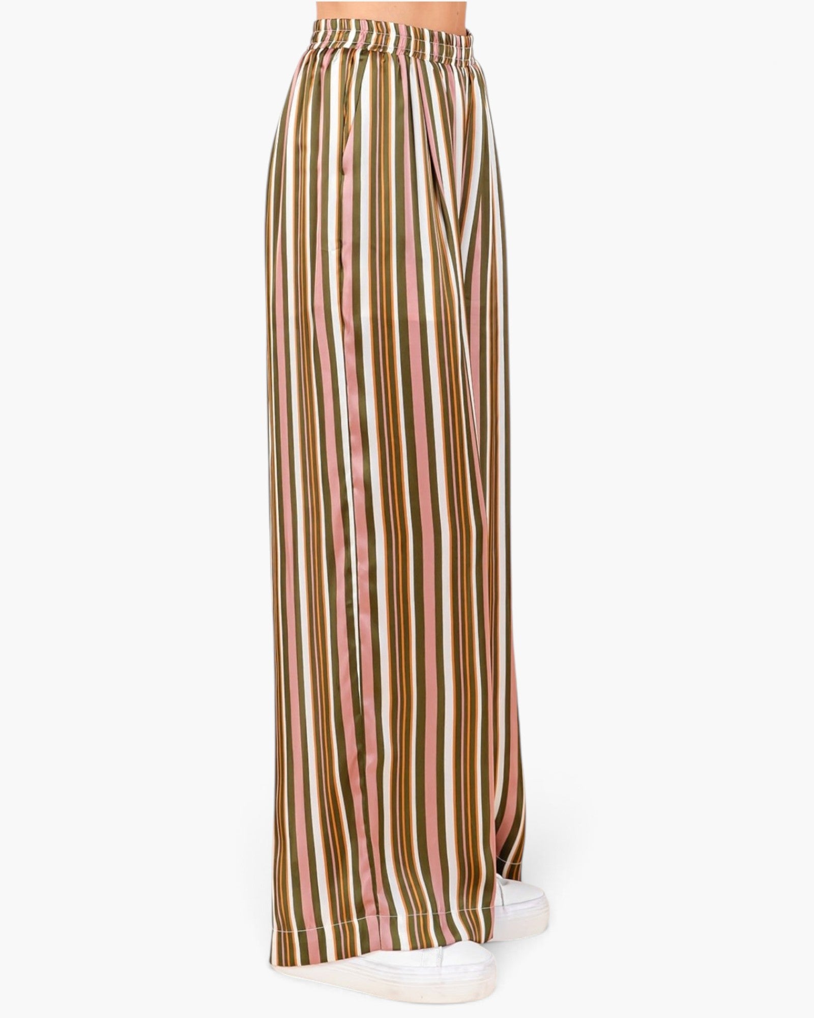 A person shown from the waist down wearing wide-leg striped pants with vertical stripes in olive green, pink, beige, and white, paired with white sneakers against a plain white background.
