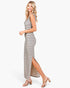 A woman modeling a sleeveless, floor-length striped maxi dress with a thigh-high slit, paired with nude block-heel sandals, against a plain white studio background.
