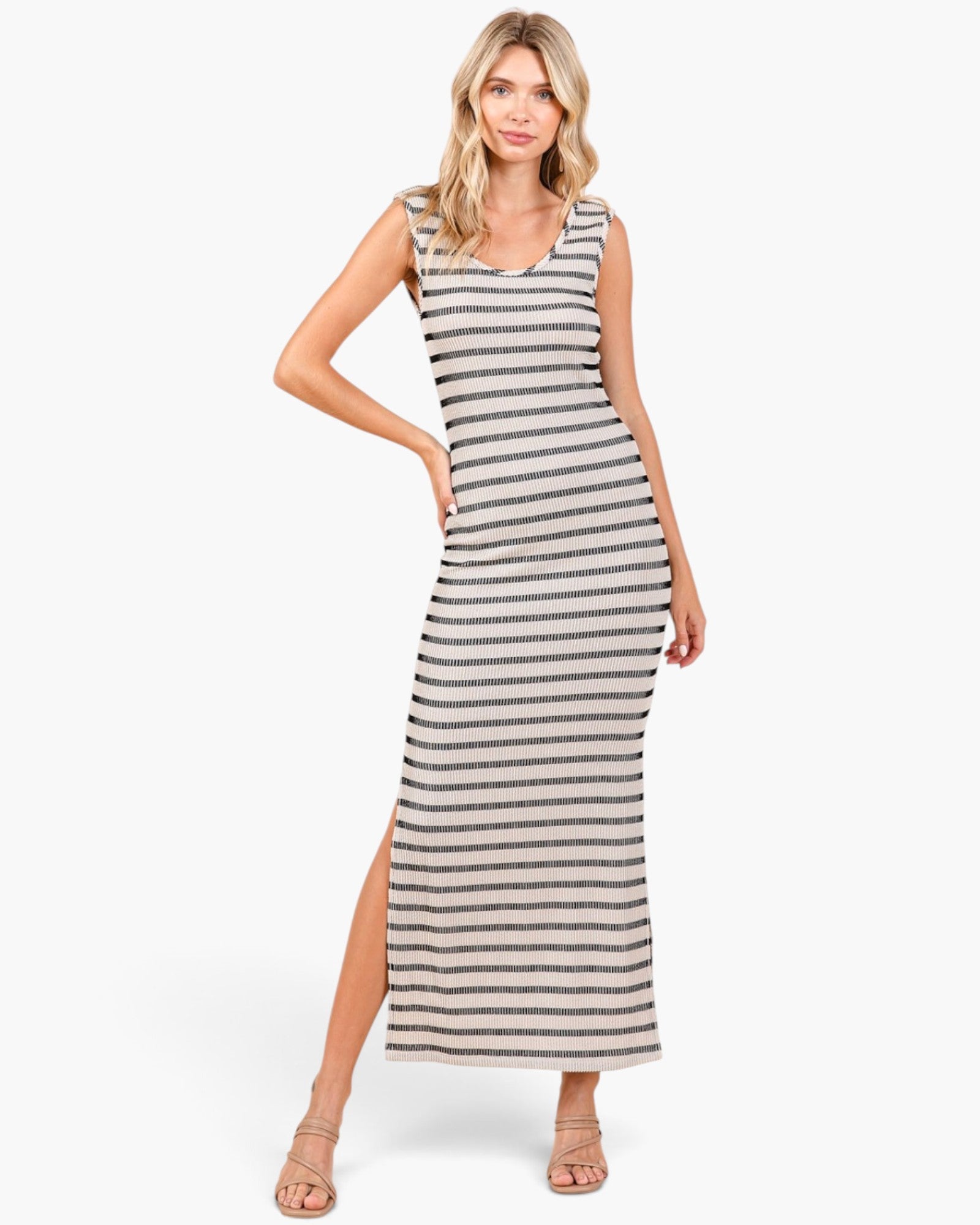 A woman modeling a sleeveless, bodycon maxi dress with horizontal beige and gray stripes, featuring a high side slit and scoop neckline, set against a plain white studio background.