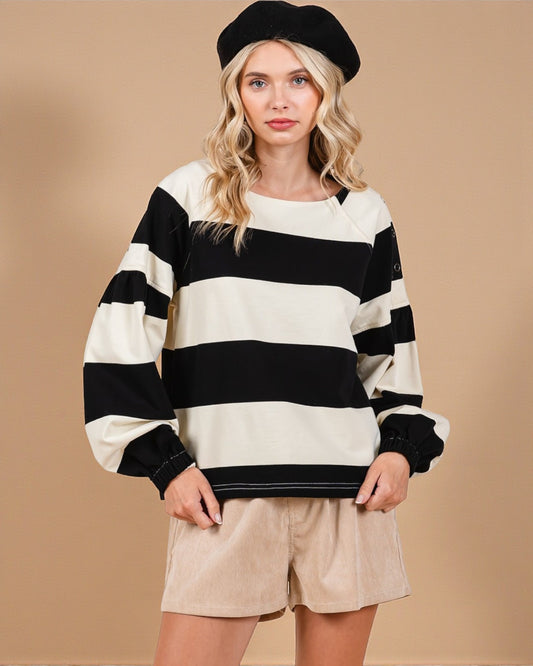 Woman wearing a black and white striped sweater with beige shorts on a beige background