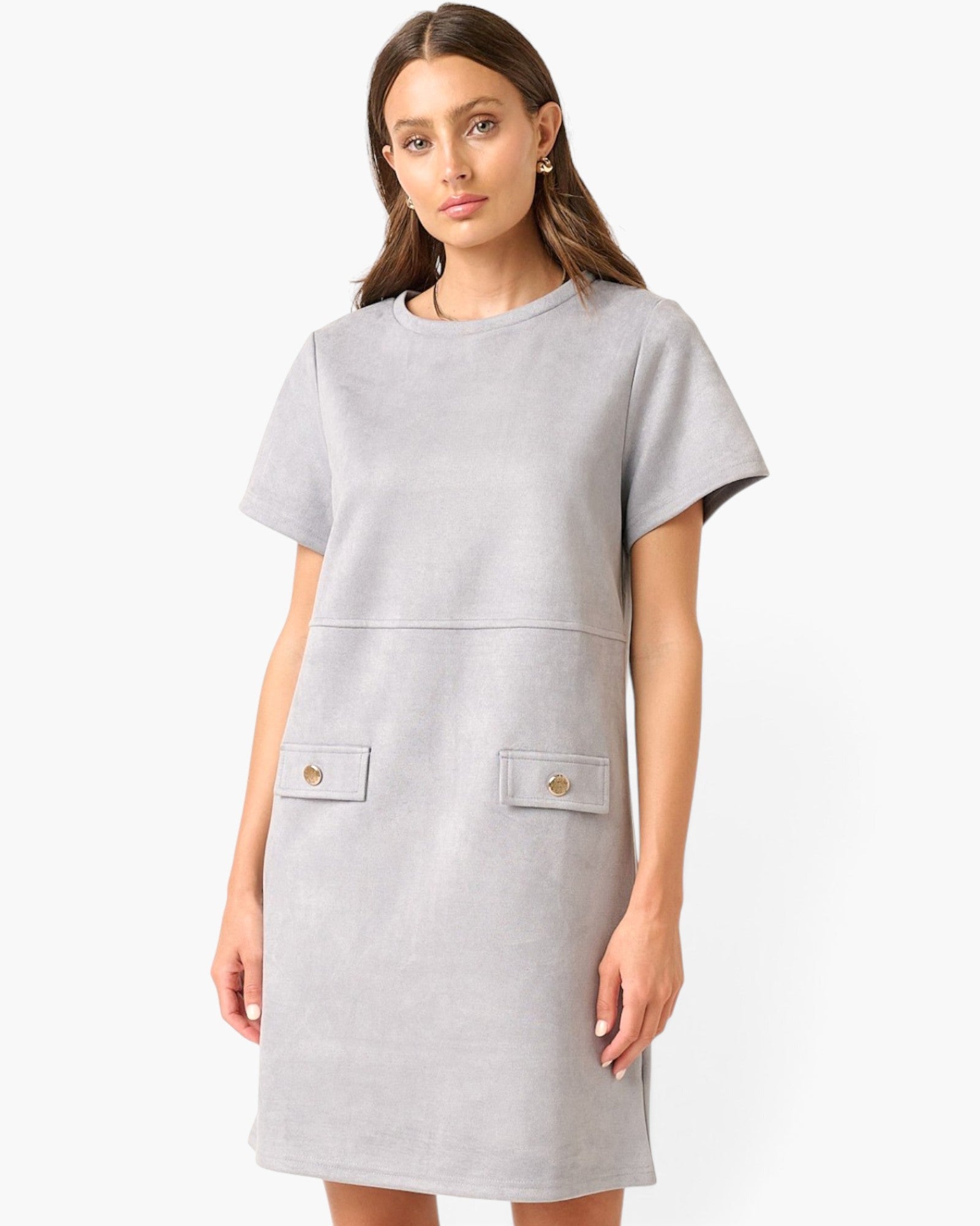 A woman modeling a light gray short-sleeve dress with two front patch pockets featuring small gold-tone buttons, photographed against a plain white studio background.