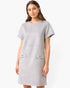 A woman modeling a light gray short-sleeve dress with two front patch pockets featuring small gold-tone buttons, photographed against a plain white studio background.
