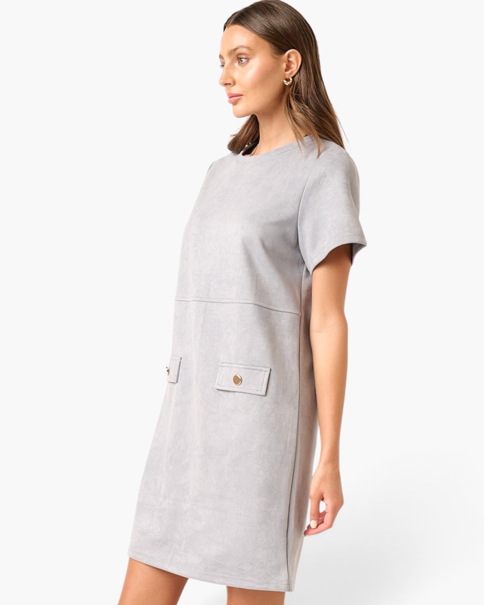 A woman wearing a light gray short-sleeve shift dress with a crew neck and two front flap pockets with gold-tone buttons, photographed against a clean white studio background.