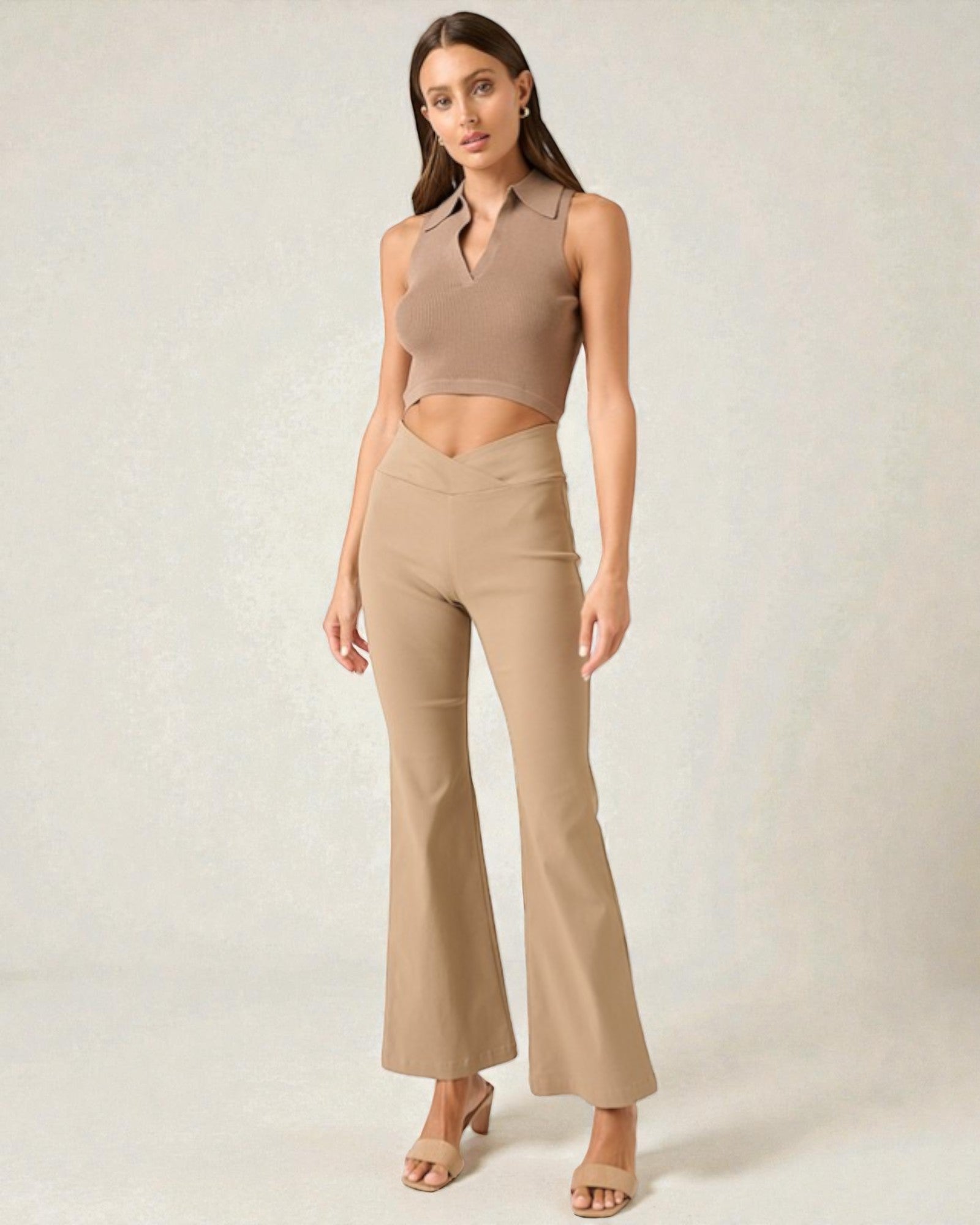 Woman wearing a beige sleeveless top and flared pants on a plain background