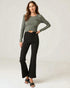 Woman wearing a green long-sleeve top and black high-waisted pants on a light gray background