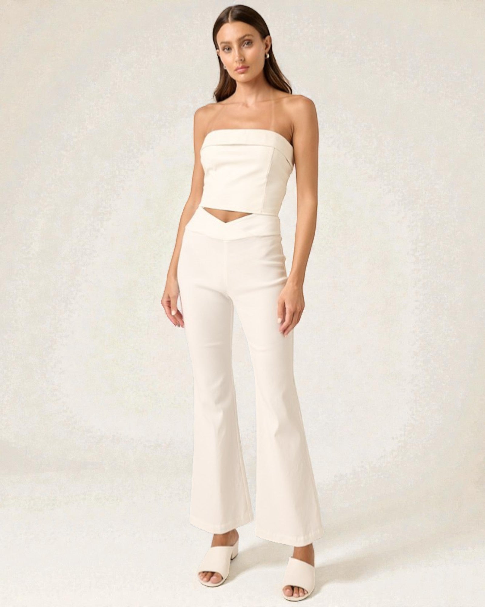 Woman wearing a white strapless top and flared pants on a plain background