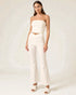 Woman wearing a white strapless top and flared pants on a plain background