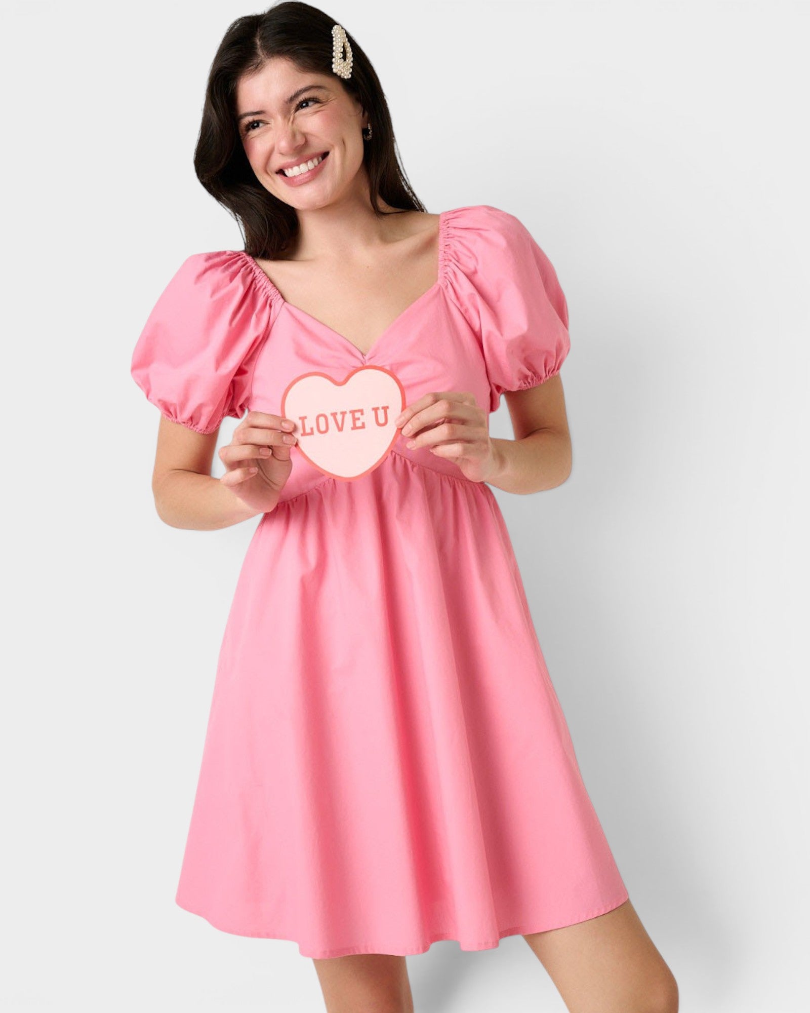 Woman wearing a pink dress holding a heart-shaped sign with 'LOVE U' on a white background