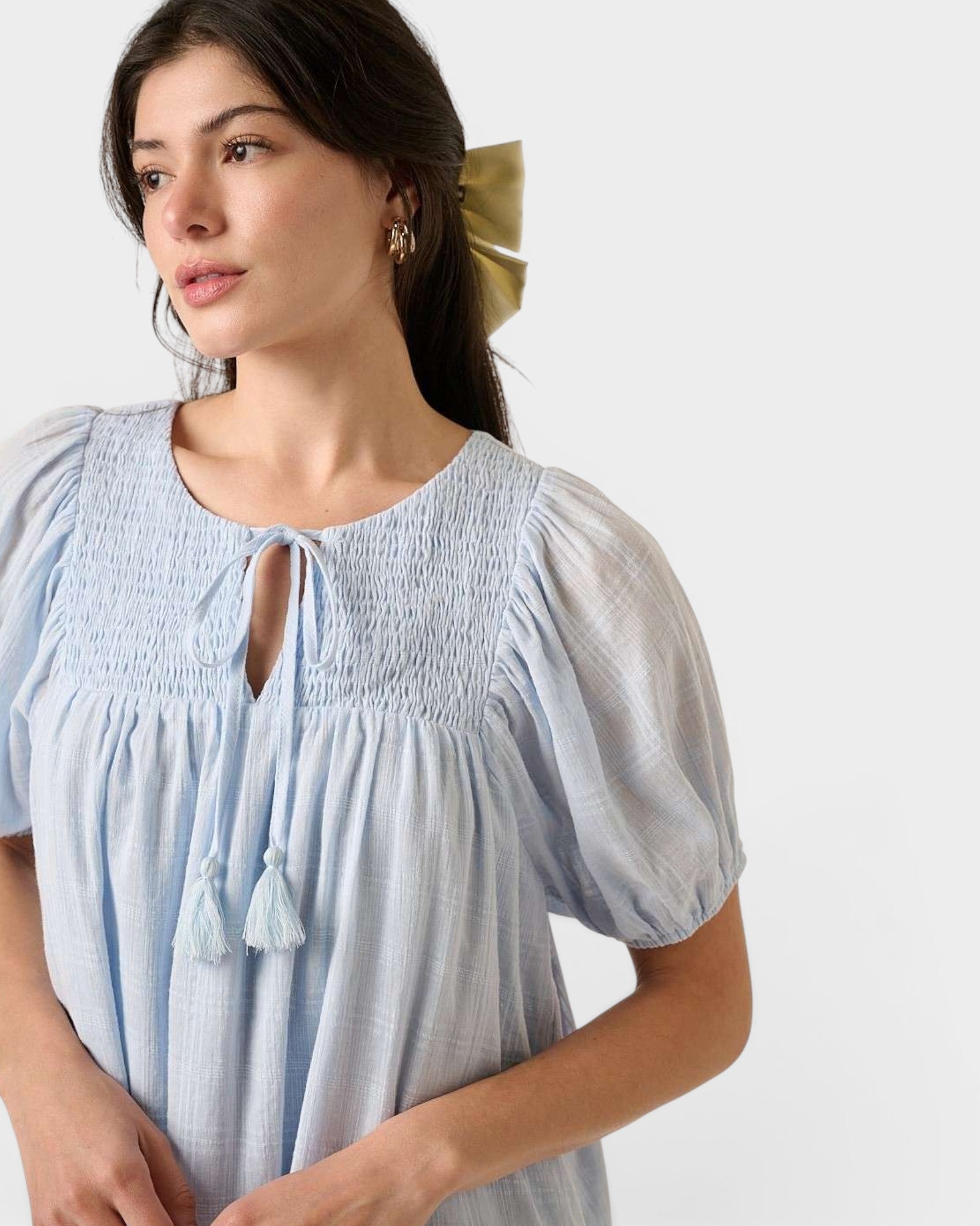 Woman wearing a light blue dress with smocked bodice and tassel details on a white background