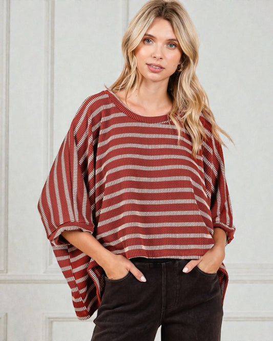 Woman wearing a red and white striped poncho against a white wall
