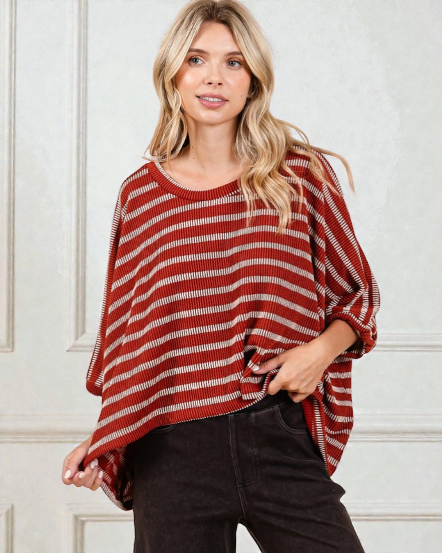 Woman wearing a red and white striped poncho against a white wall