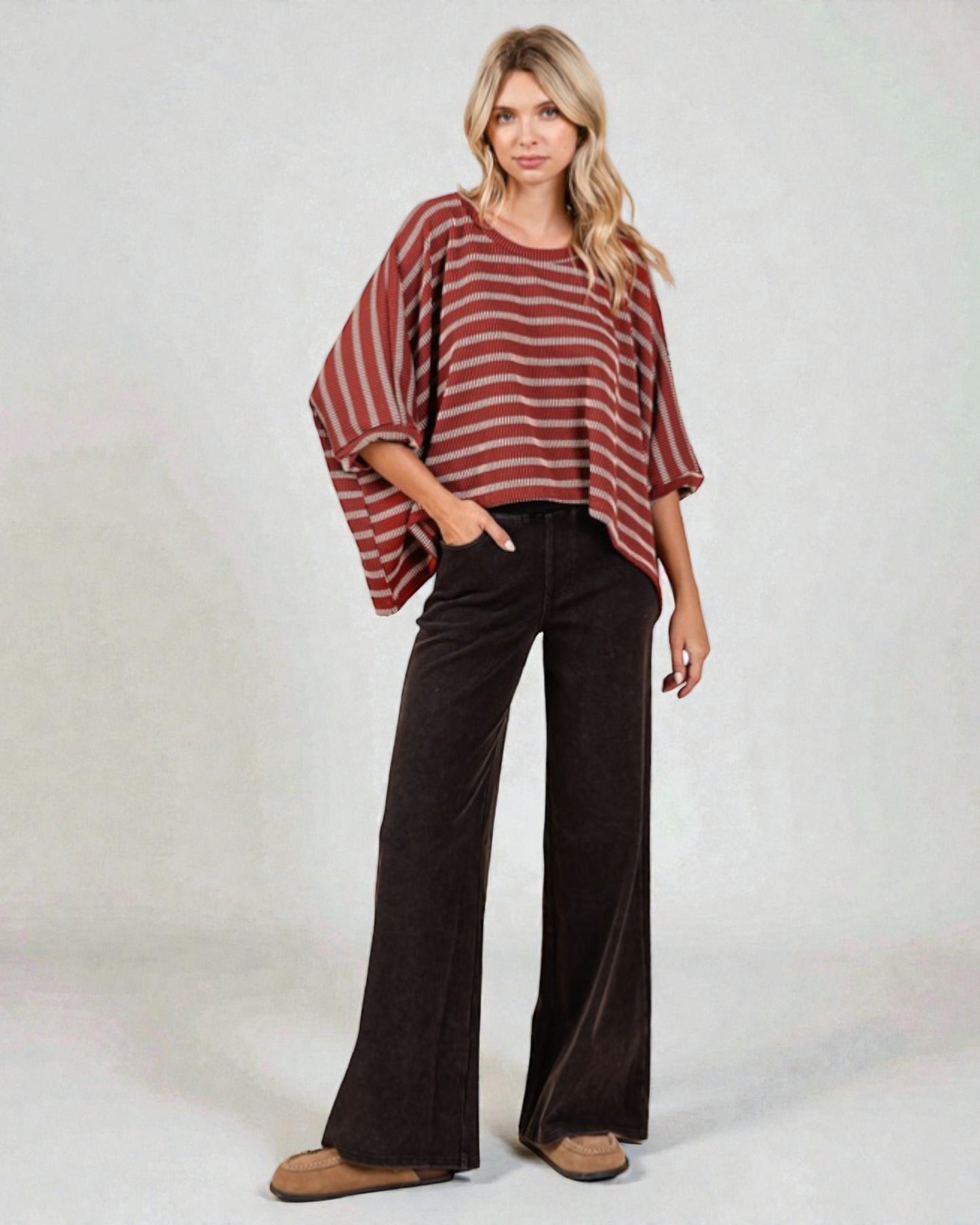 Woman wearing a striped top and wide-leg pants on a plain background