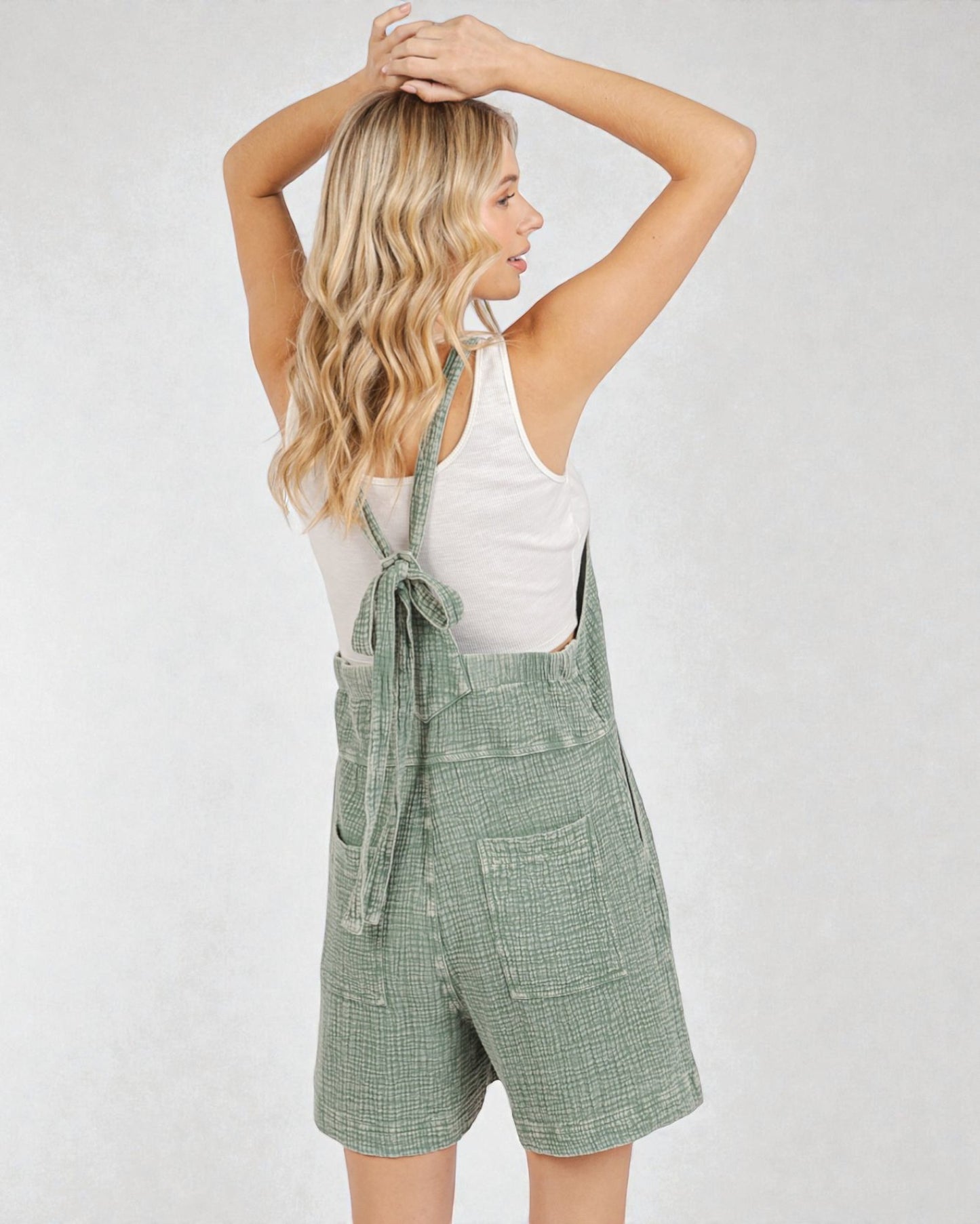 Woman wearing green checkered overalls and a white top on a plain background