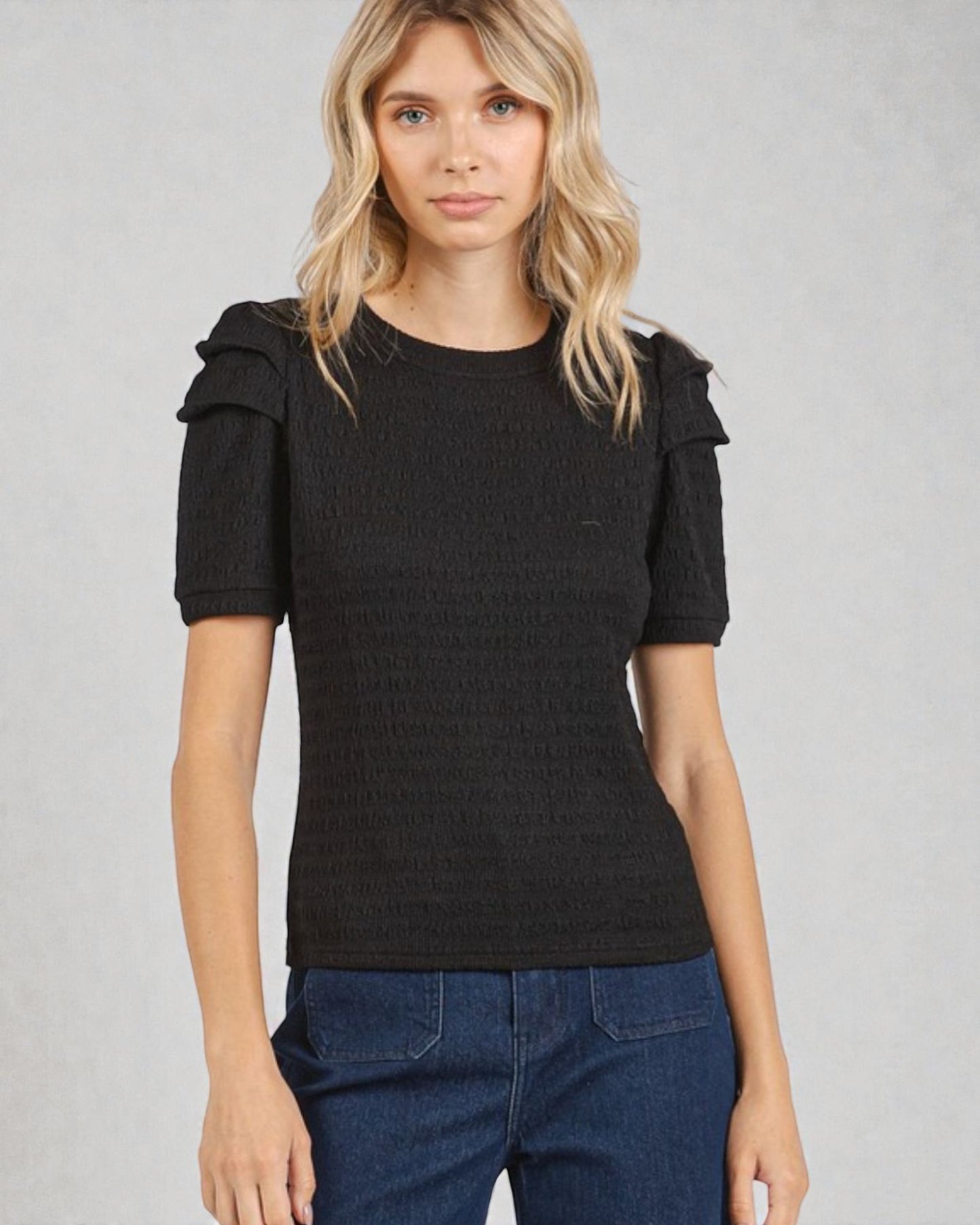 Woman wearing a black top with ruffled sleeves against a gray background