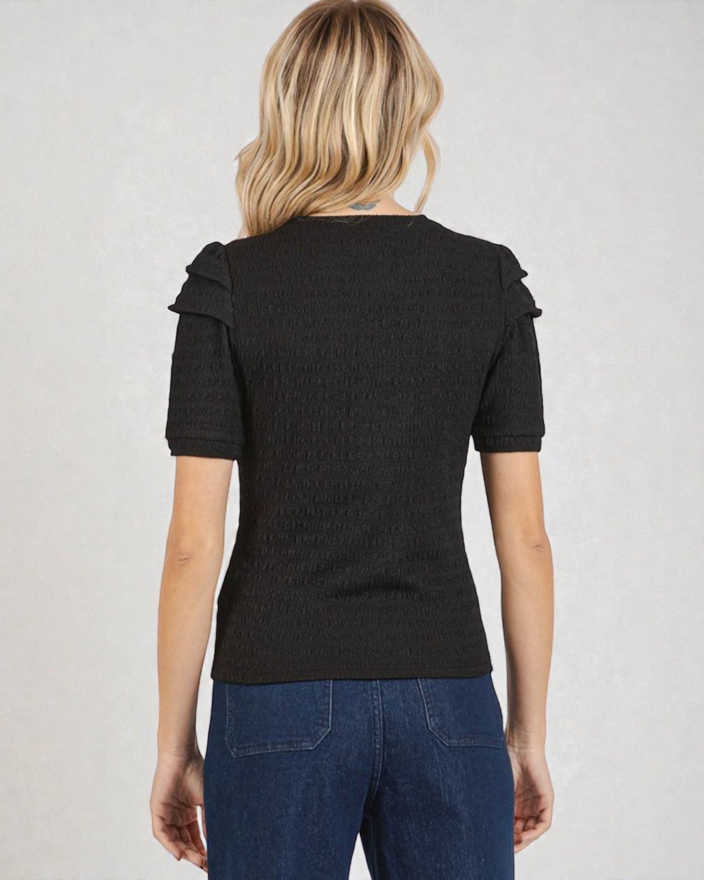 Person wearing a black ruffled top and blue jeans on a plain background