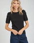 Woman wearing a black textured top with ruffled sleeves against a plain background