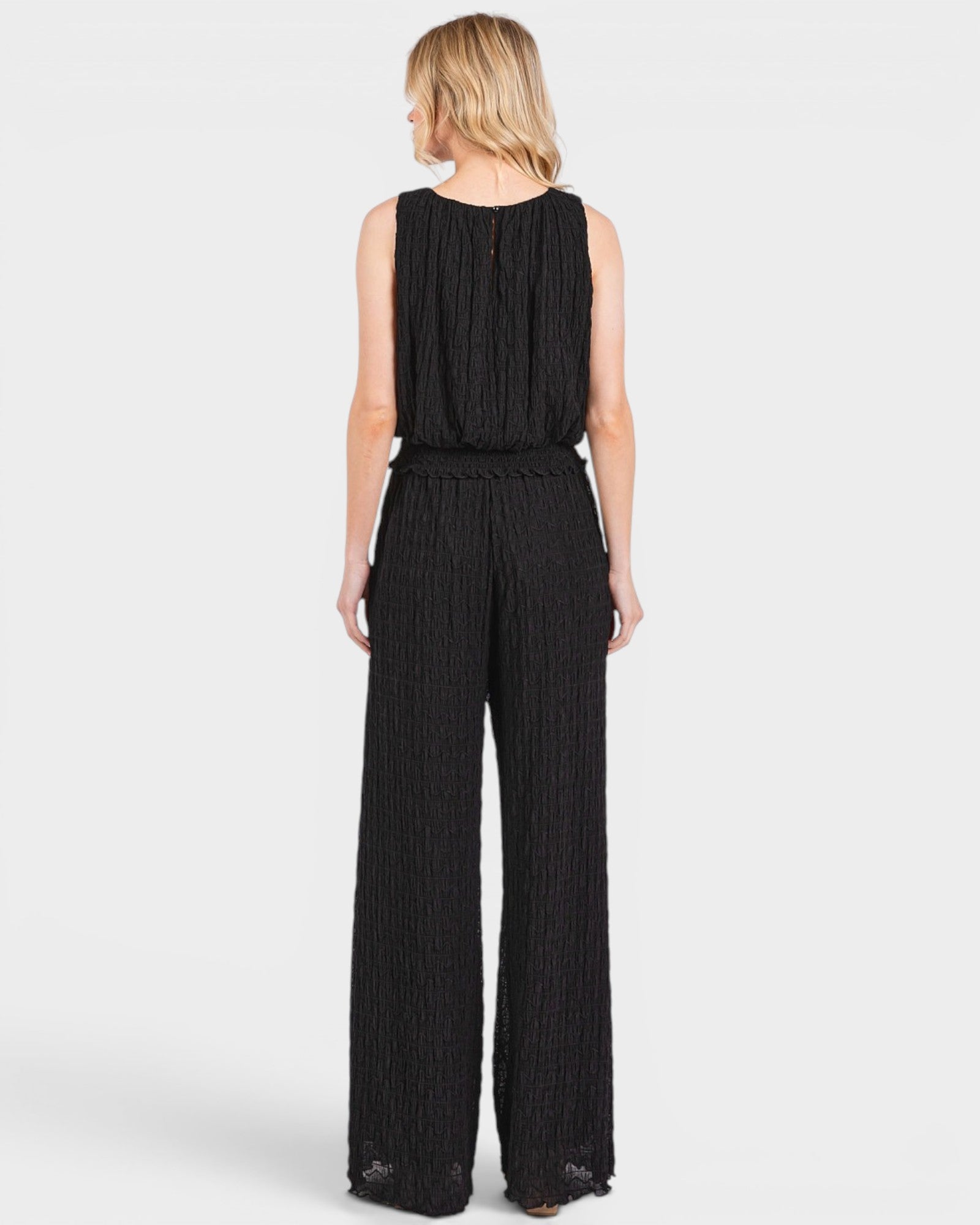Woman wearing a black sleeveless top and wide-leg pants on a white background