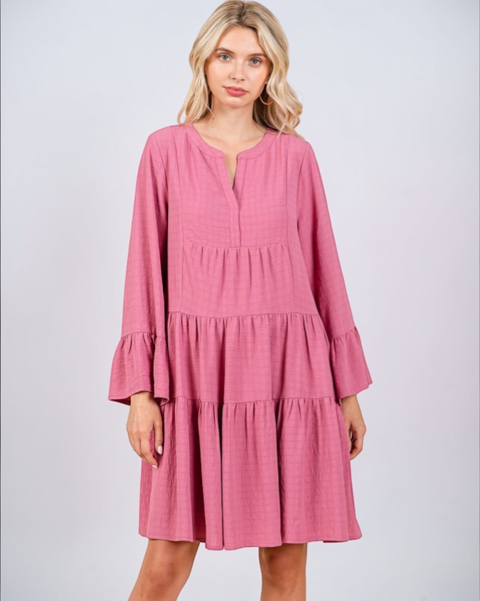 Woman wearing a pink dress with long sleeves on a light gray background