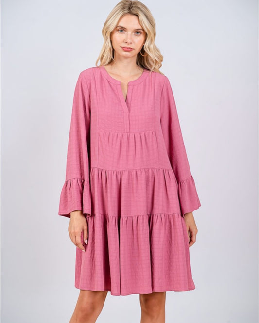 Woman wearing a pink dress with long sleeves on a light gray background