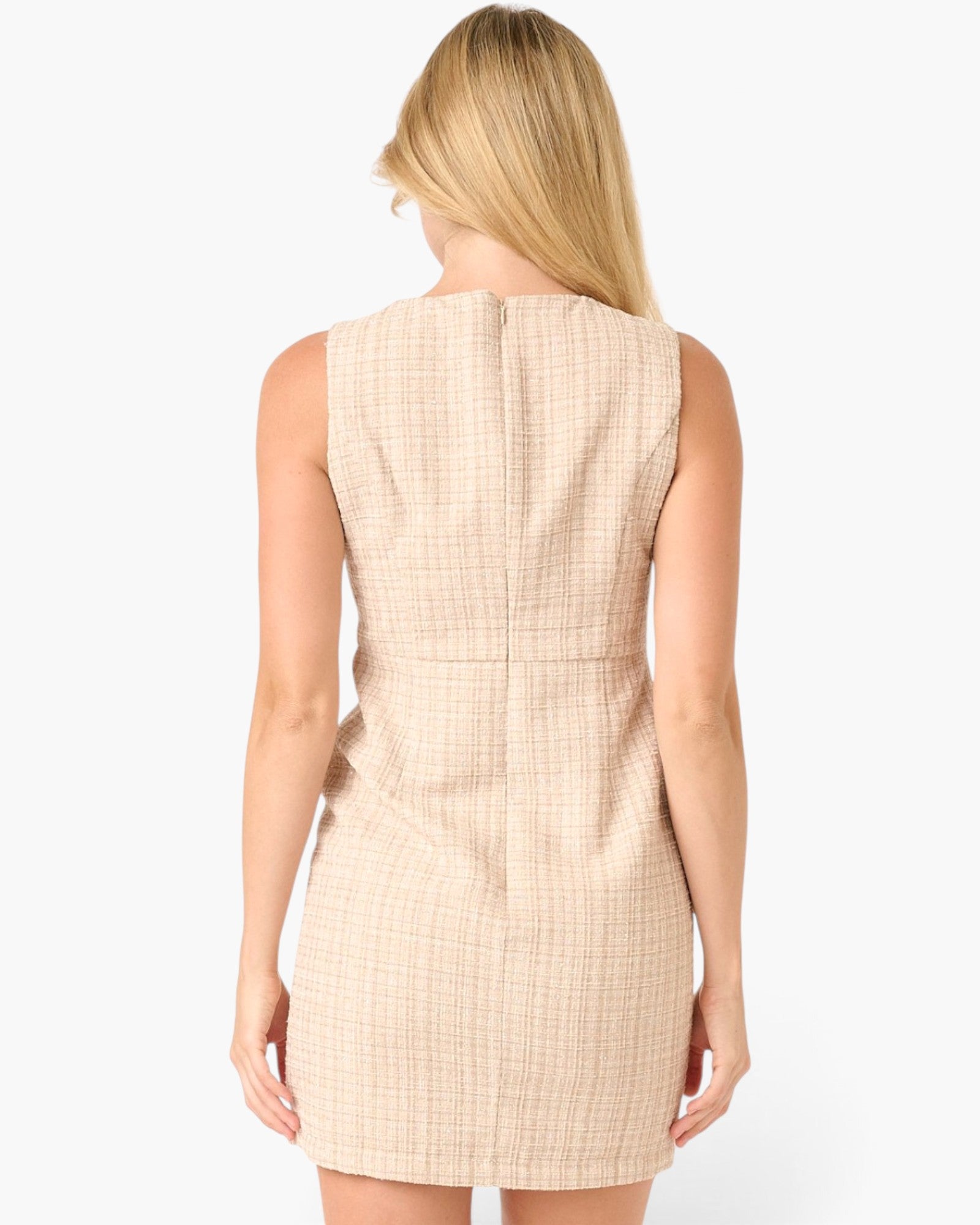 A woman viewed from the back wearing a sleeveless beige dress with a subtle grid pattern, set against a plain white studio background.