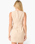 A woman viewed from the back wearing a sleeveless beige dress with a subtle grid pattern, set against a plain white studio background.