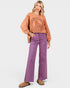 Woman wearing a brown sweatshirt with a peace sign design and purple pants on a white background