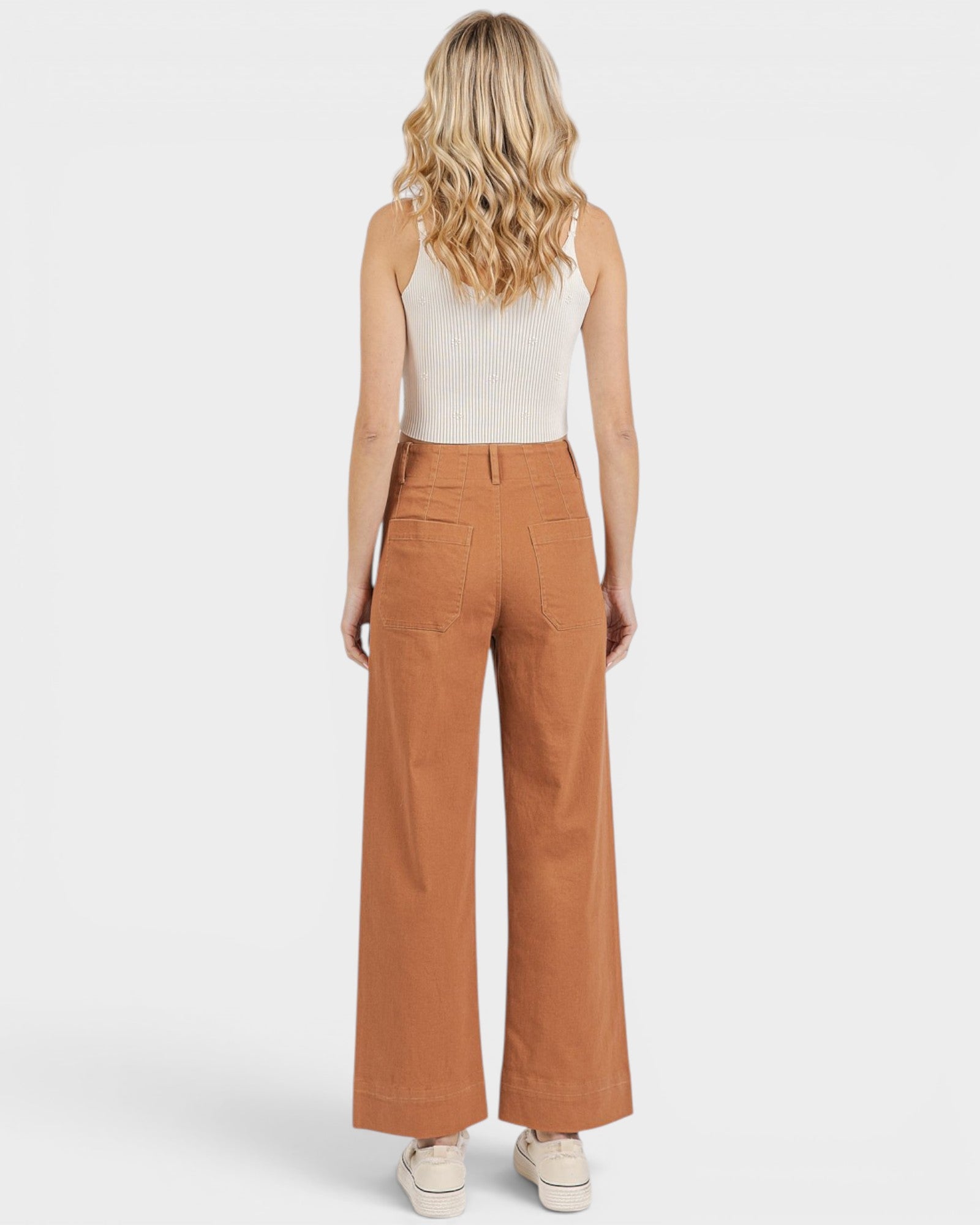 Woman wearing brown wide-leg pants and a white top on a light gray background