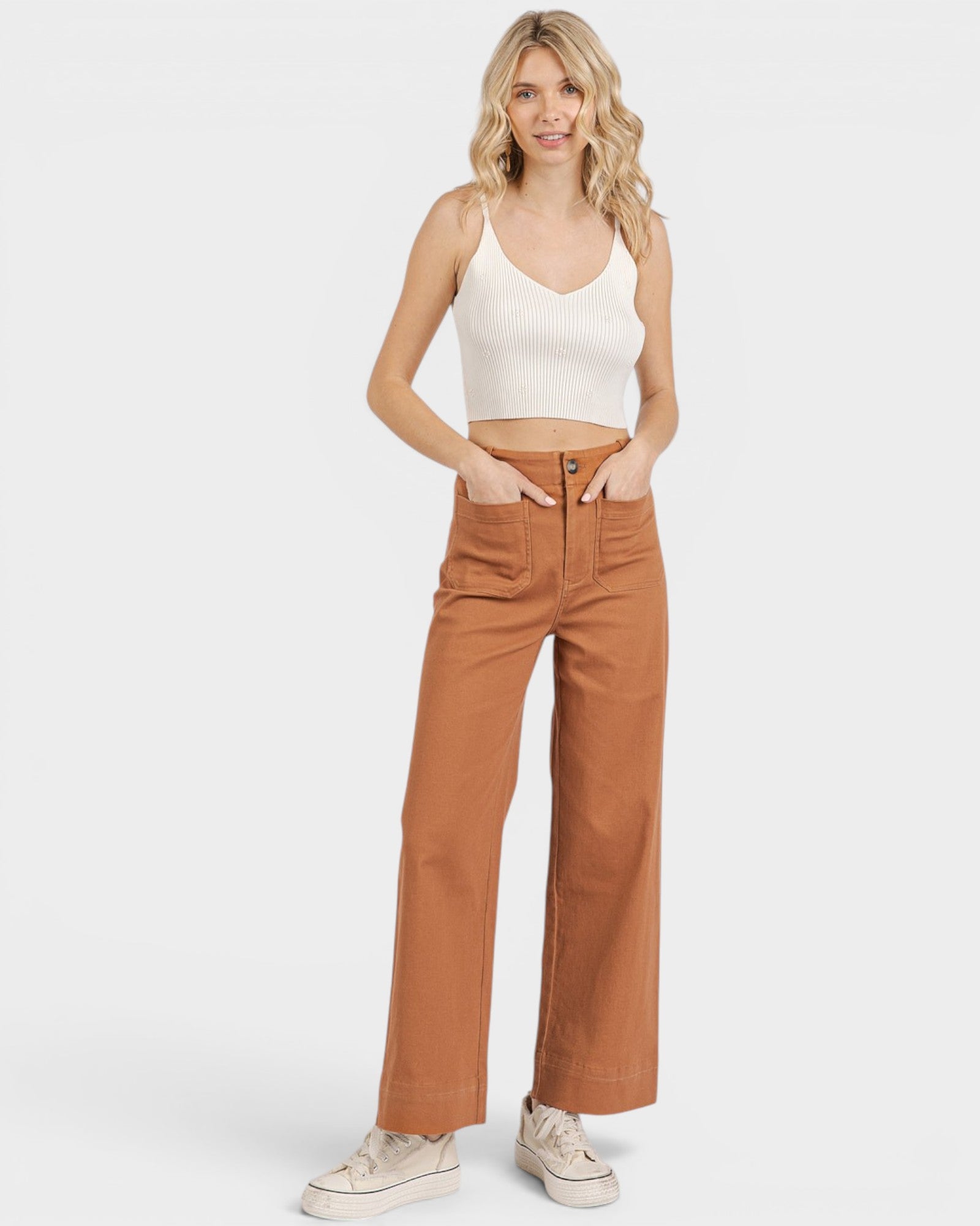 Woman wearing a white tank top and brown high-waisted pants on a white background