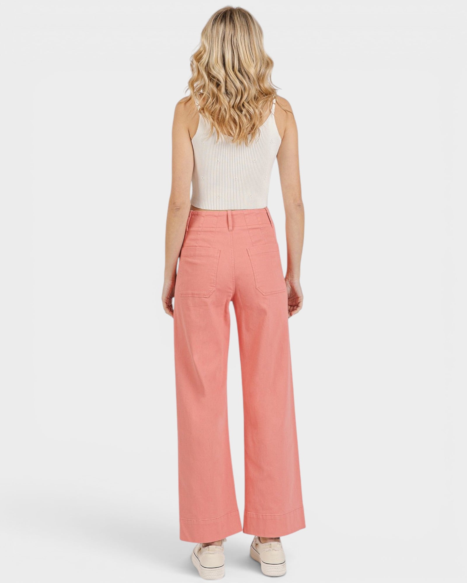 Woman wearing coral pants and a white top on a light gray background