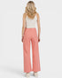 Woman wearing coral pants and a white top on a light gray background