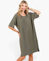 A woman modeling an oversized short-sleeve knit dress in olive green against a plain white studio background.