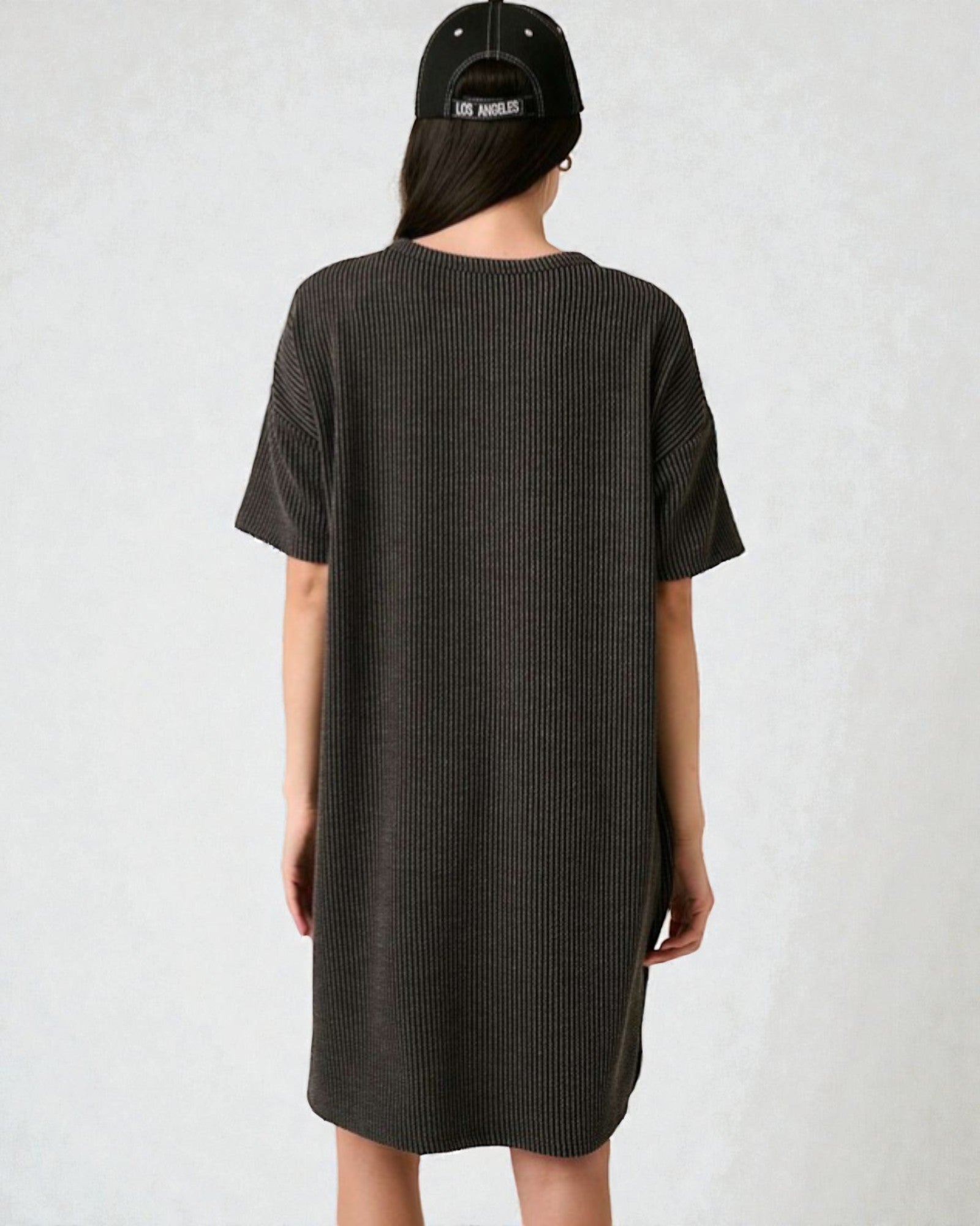 Person wearing a black t-shirt dress and cap on a white background