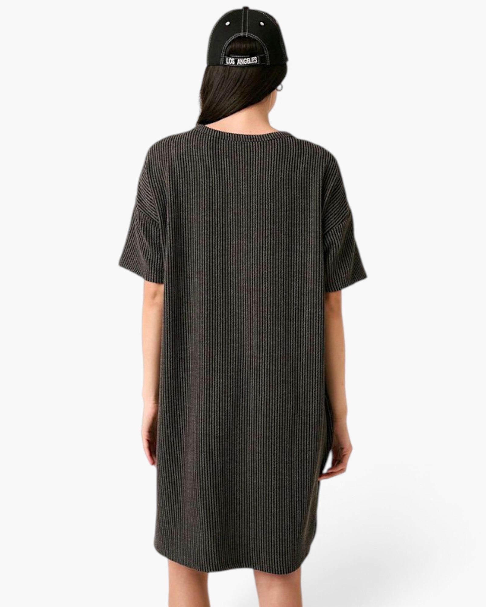 A person shown from the back wearing a dark charcoal gray ribbed short-sleeve dress and a black baseball cap with white text, against a plain white studio background.