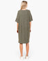 A woman viewed from the back wearing an oversized short-sleeve knit dress in olive green, paired with white sneakers, against a plain white studio background.