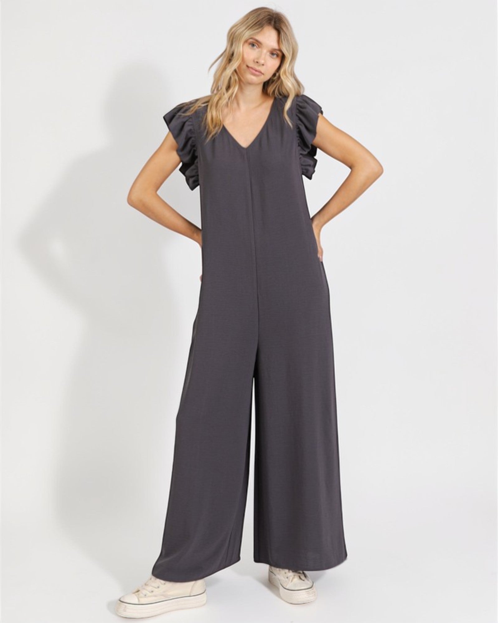 Woman wearing a gray jumpsuit with ruffled sleeves on a white background