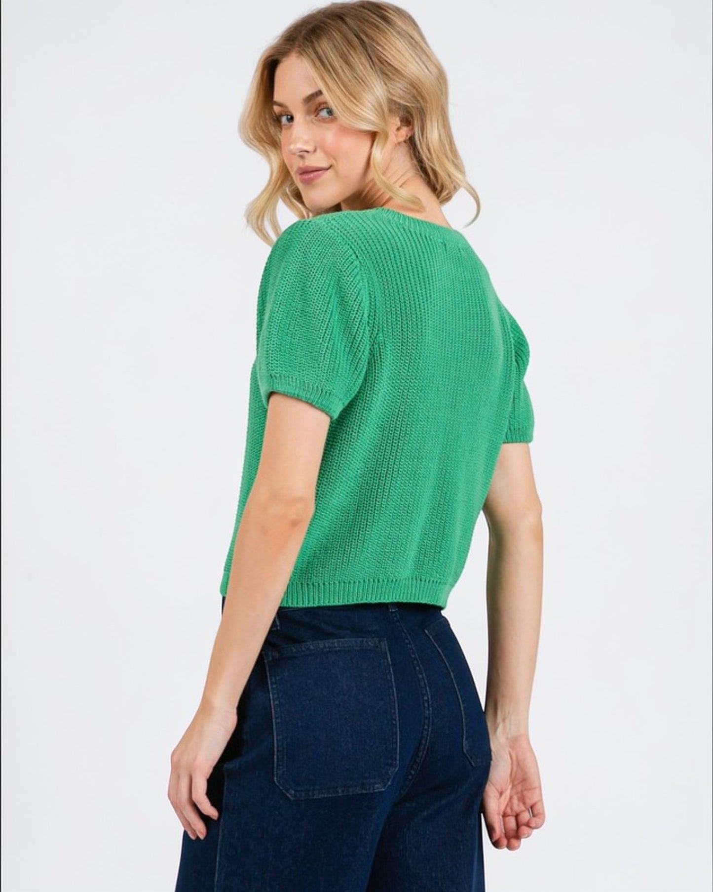 Woman wearing a green knitted top and blue jeans on a white background