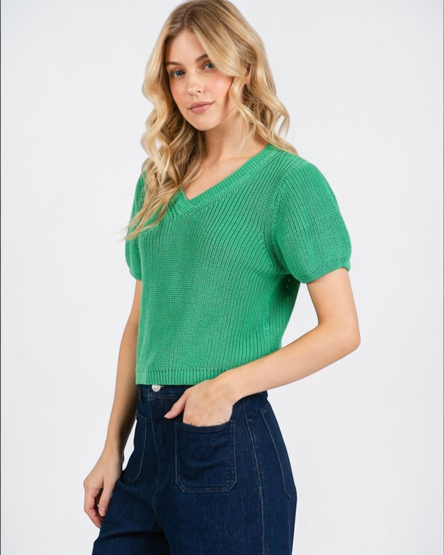 Woman wearing a green knitted top and blue jeans on a white background