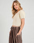 Woman wearing a cream knit top and brown wide-leg pants on a light gray background