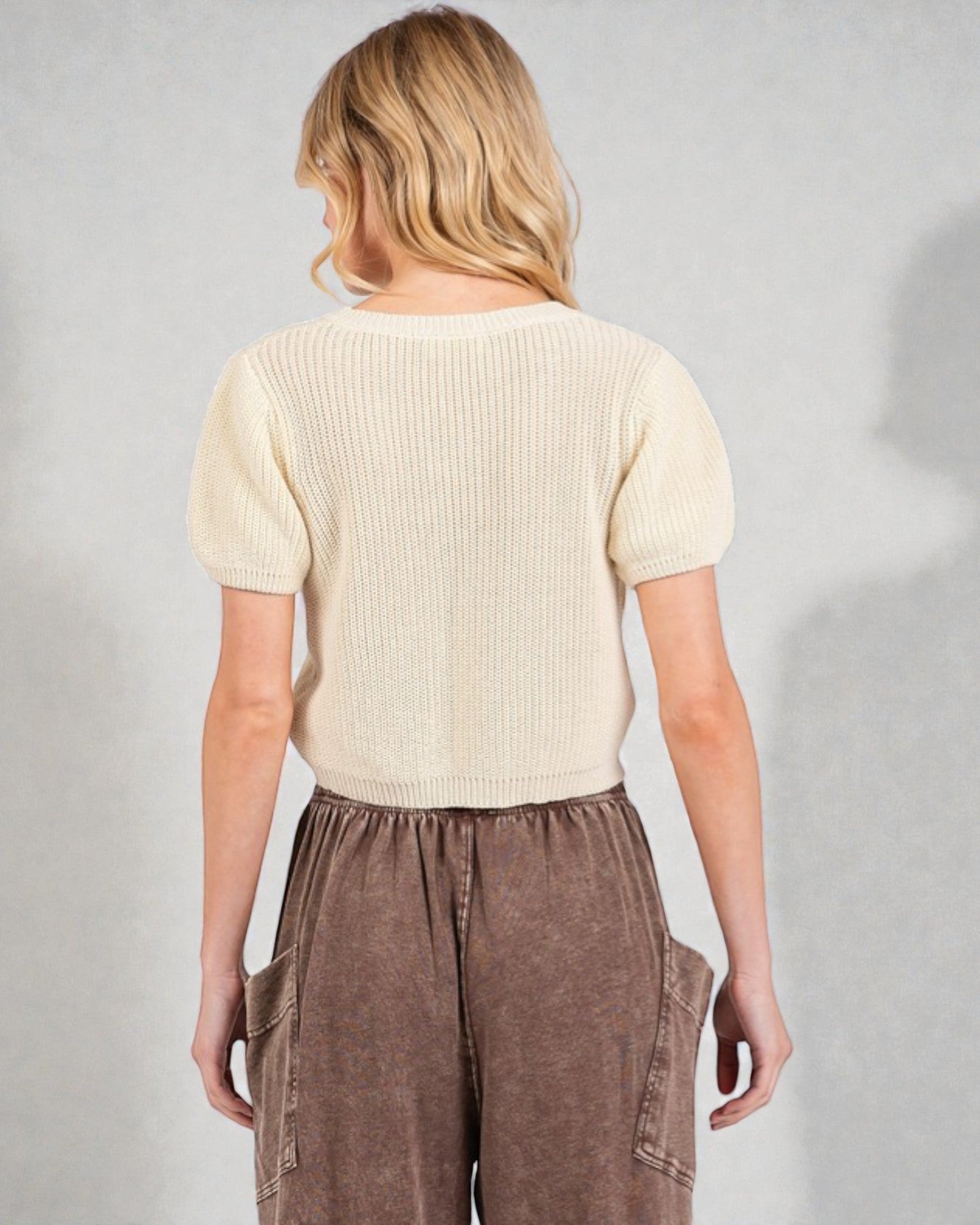 Person wearing a beige ribbed sweater and brown pants against a plain background