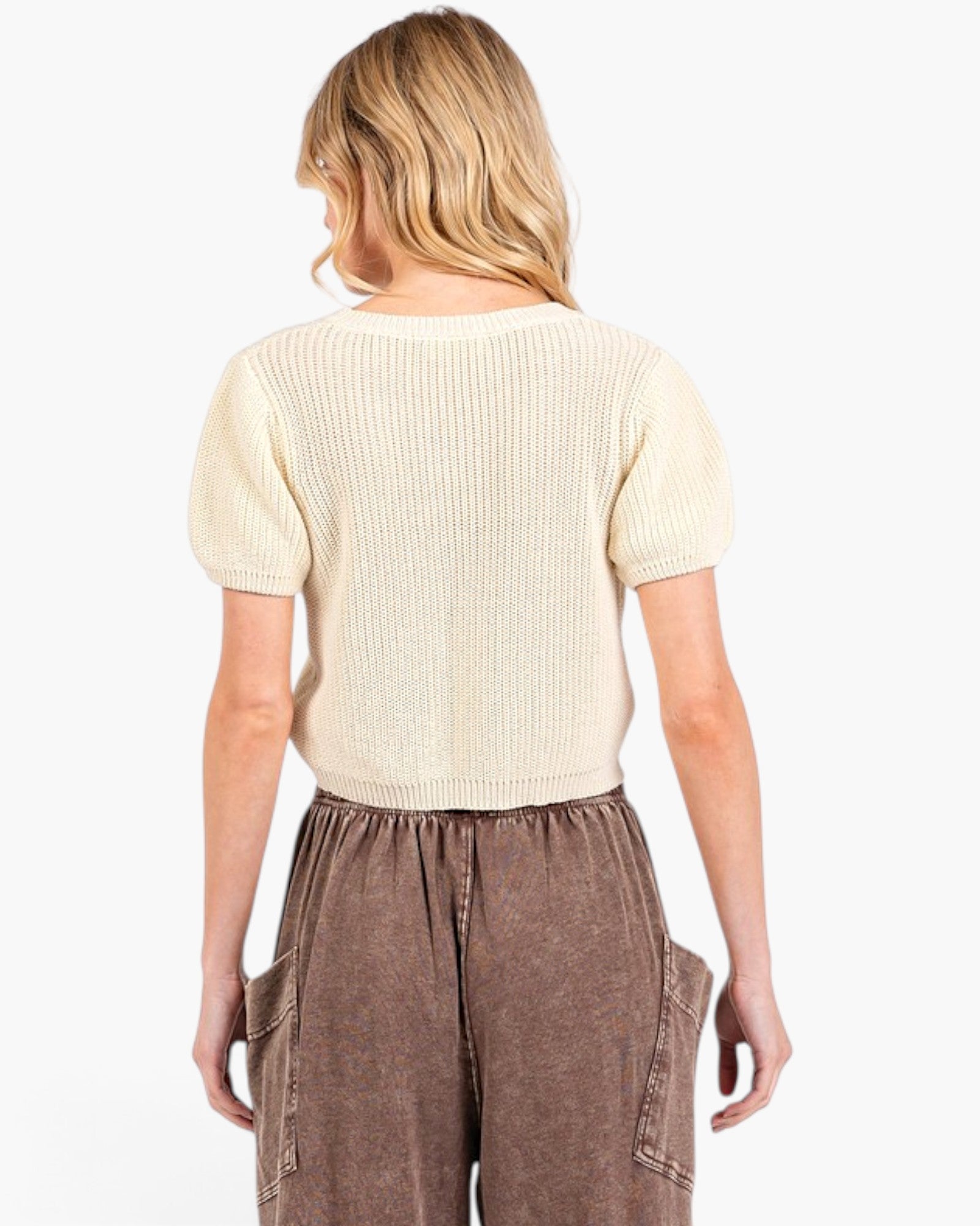 A woman shown from the back wearing a cream-colored short-sleeve ribbed knit top and brown wide-leg pants against a plain white background.