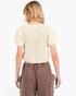 A woman shown from the back wearing a cream-colored short-sleeve ribbed knit top and brown wide-leg pants against a plain white background.