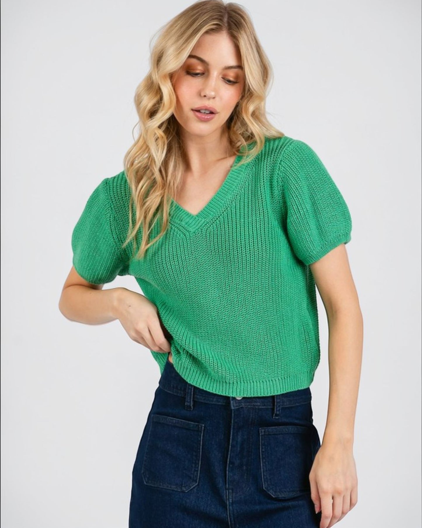 Woman wearing a green knitted top and dark blue jeans on a white background