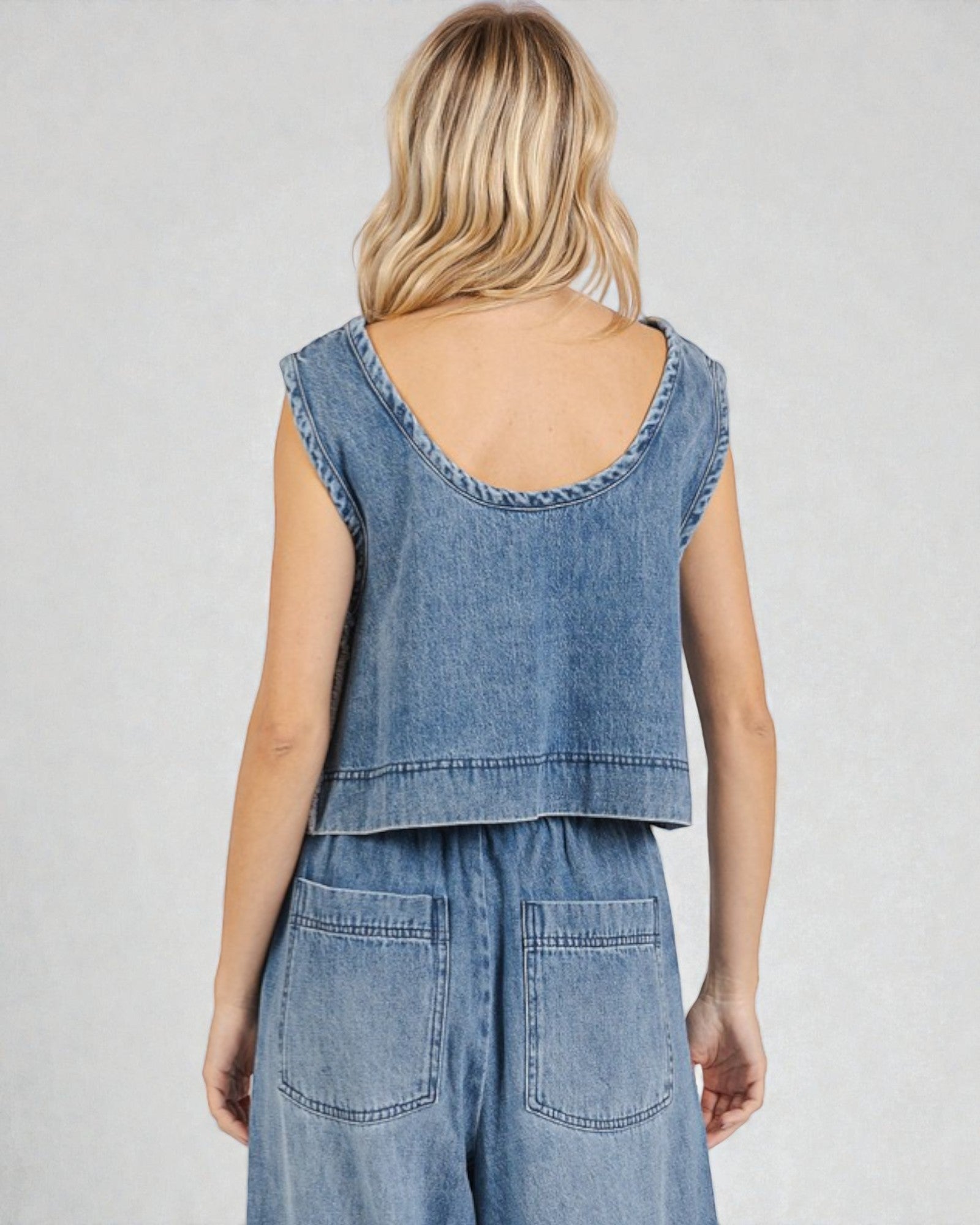 Woman wearing a denim sleeveless top and pants on a plain background
