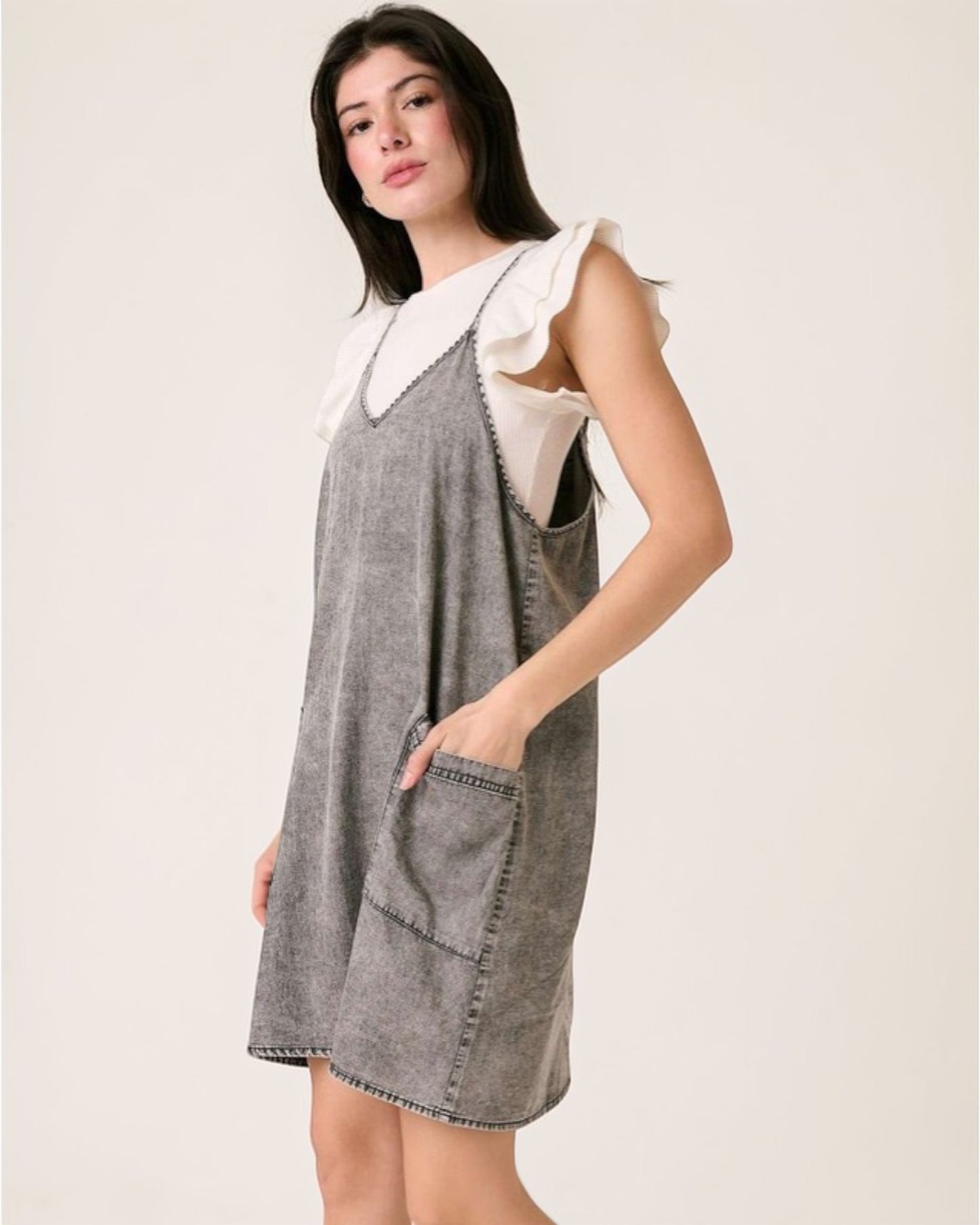 Woman wearing a gray denim dress with a white ruffled top on a plain background