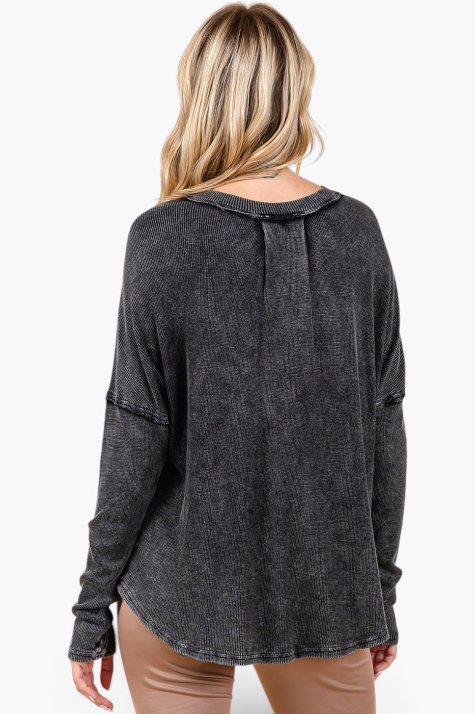 A woman viewed from the back wearing a dark charcoal gray, acid-washed long-sleeve top and tan pants against a plain white background.
