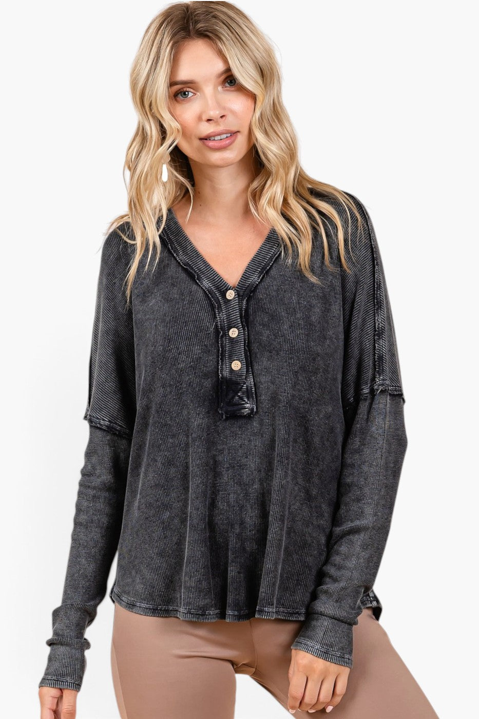 A woman wearing a dark gray mineral-wash long-sleeve henley top with gold buttons, paired with beige pants, against a plain white background.