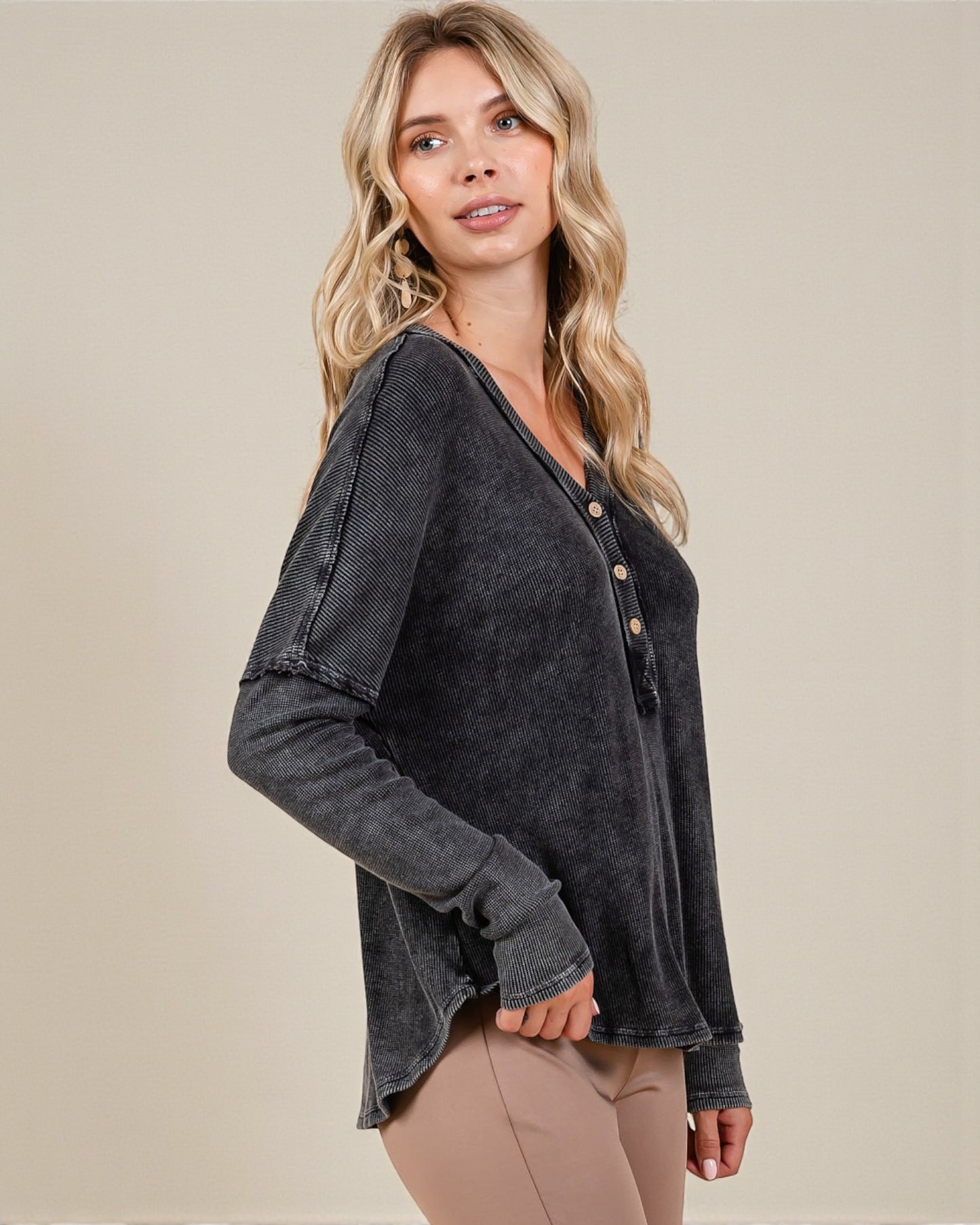 Woman wearing a dark gray long-sleeve top with button details on a beige background