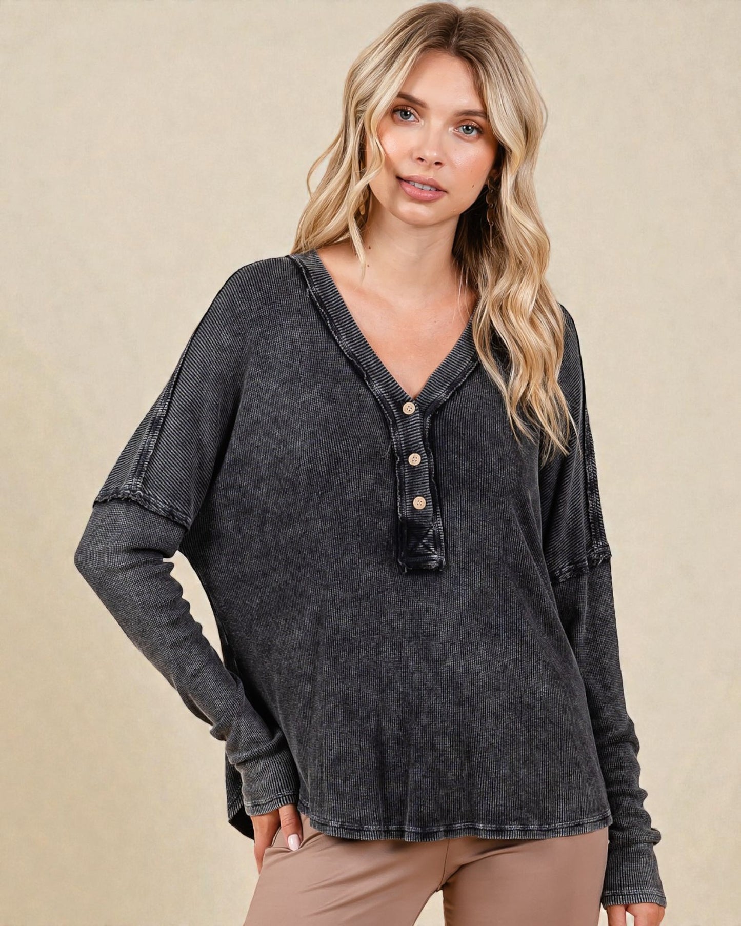 Woman wearing a dark gray long-sleeve shirt with buttons on a beige background